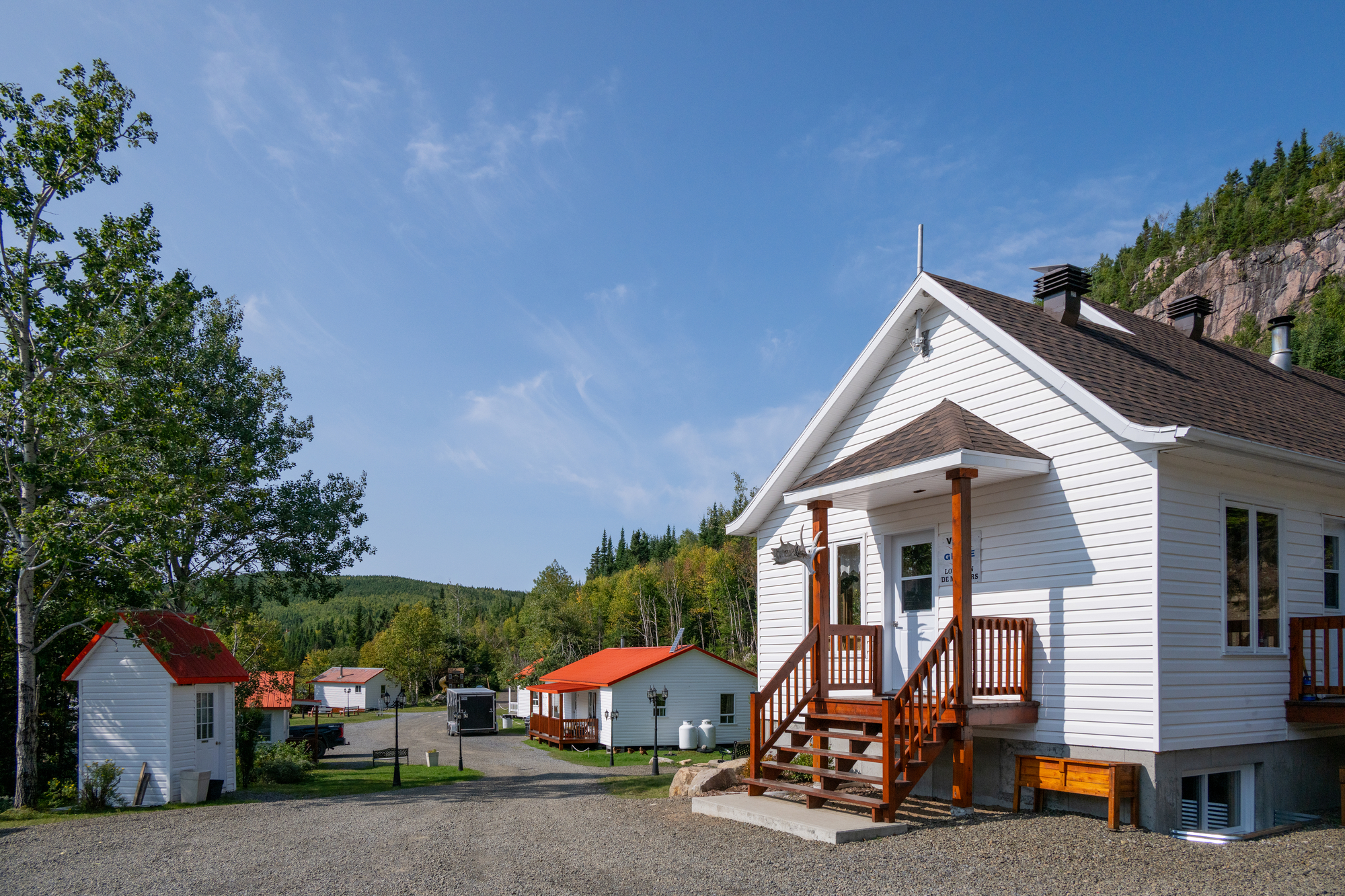 Chalets blancs au Club des Trois Castors, entourés de verdure et de montagnes sous un ciel bleu dégagé