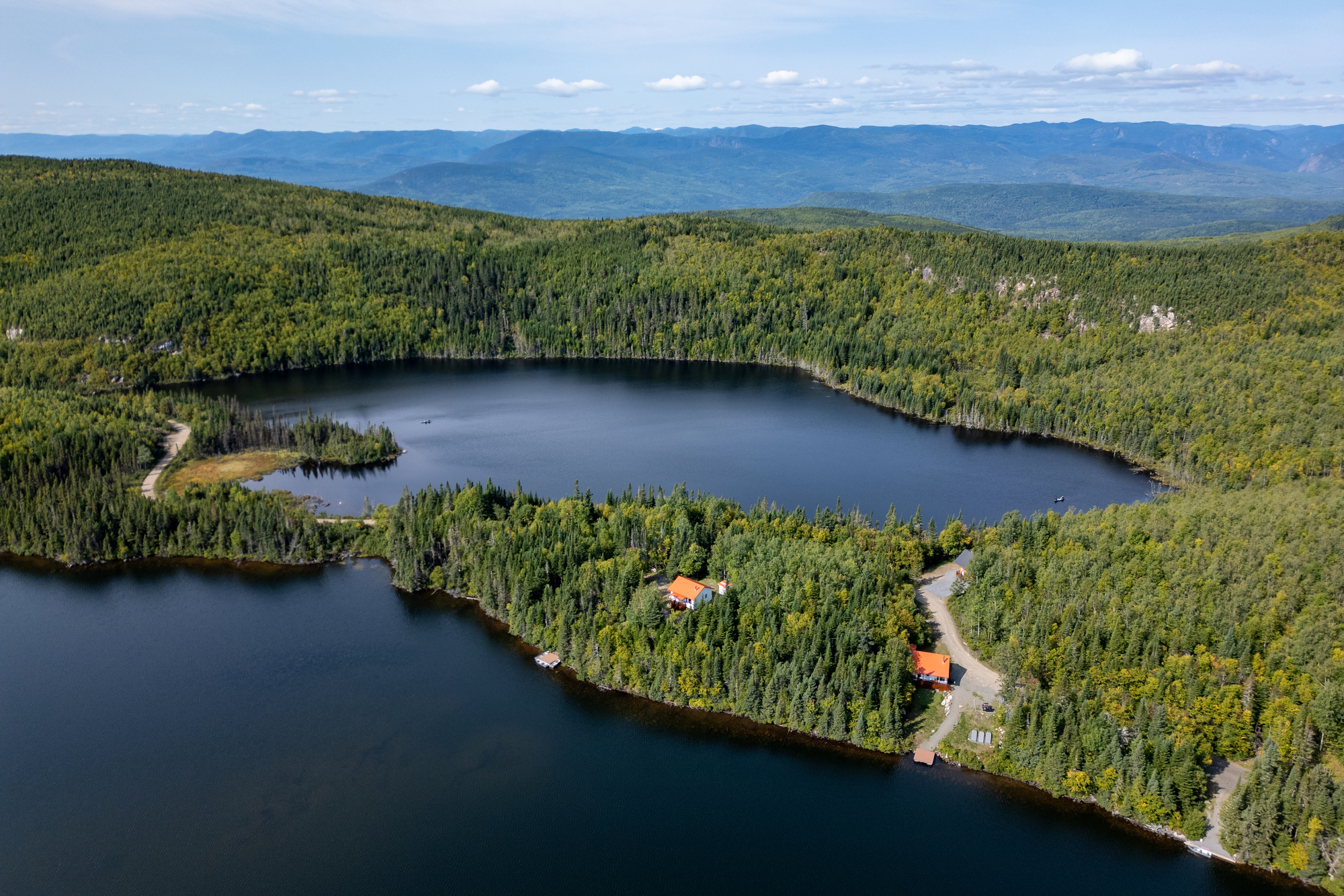 Aerial view of a serene lake surrounded by lush forest and a cozy lodge at Club des Trois Castors in Quebec