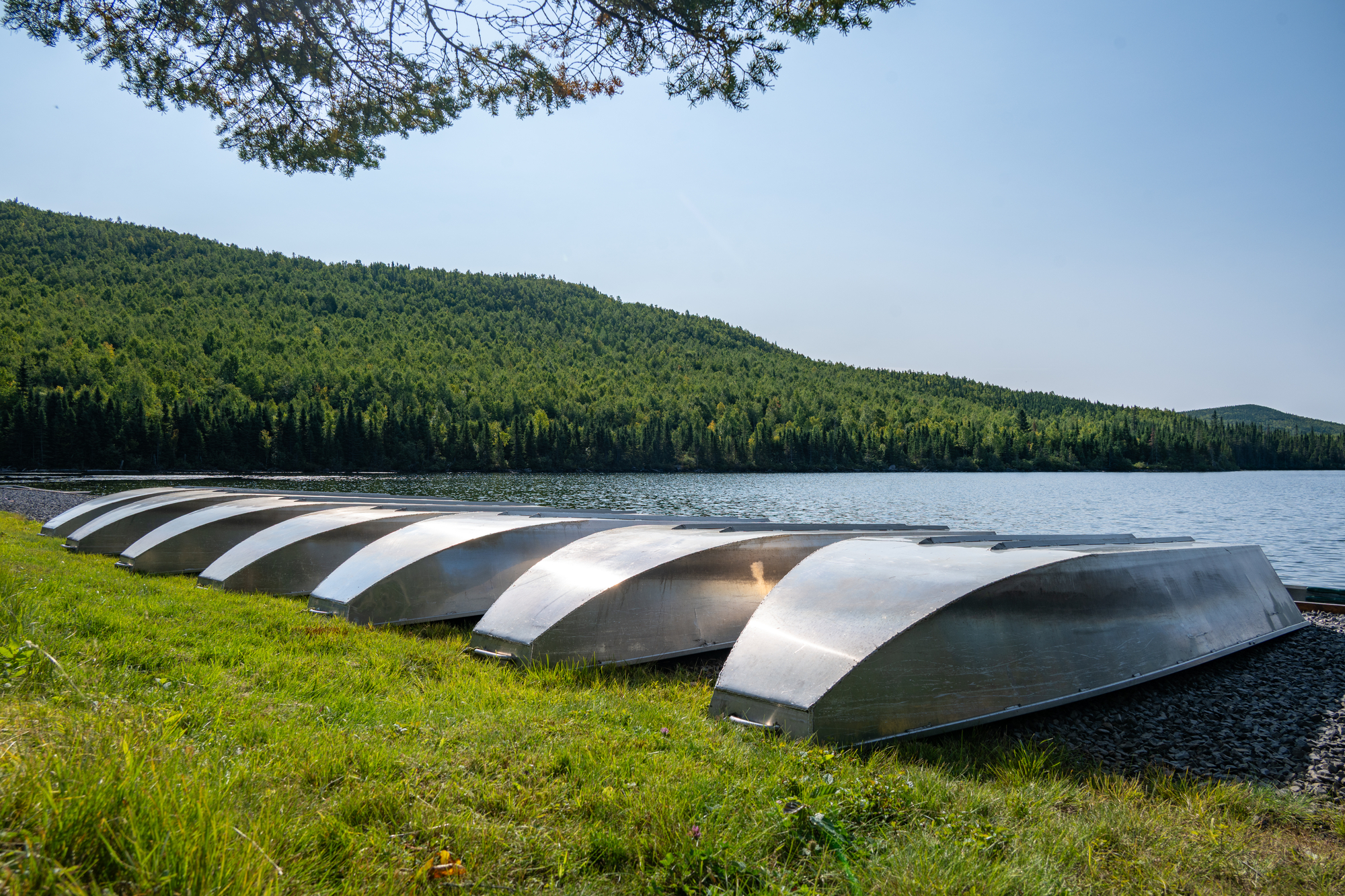 Bateaux en métal rangés sur l'herbe près d'un lac entouré de collines verdoyantes au Club des Trois Castors