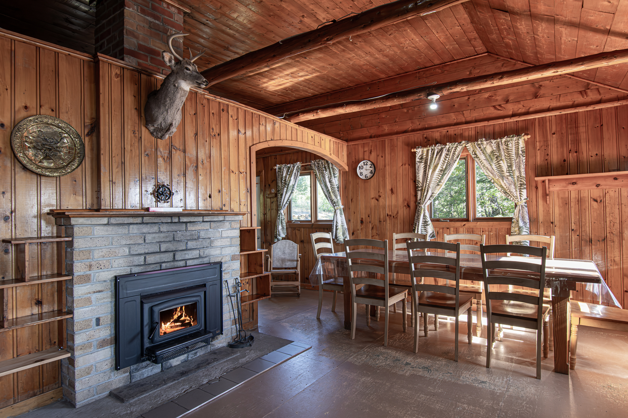 Intérieur chaleureux d'un chalet en bois avec table à manger, chaises, poêle à bois et fenêtres lumineuses dans la forêt