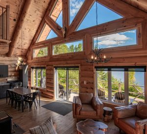 Intérieur d'un chalet en bois avec grandes fenêtres, salon confortable et vue sur la nature environnante