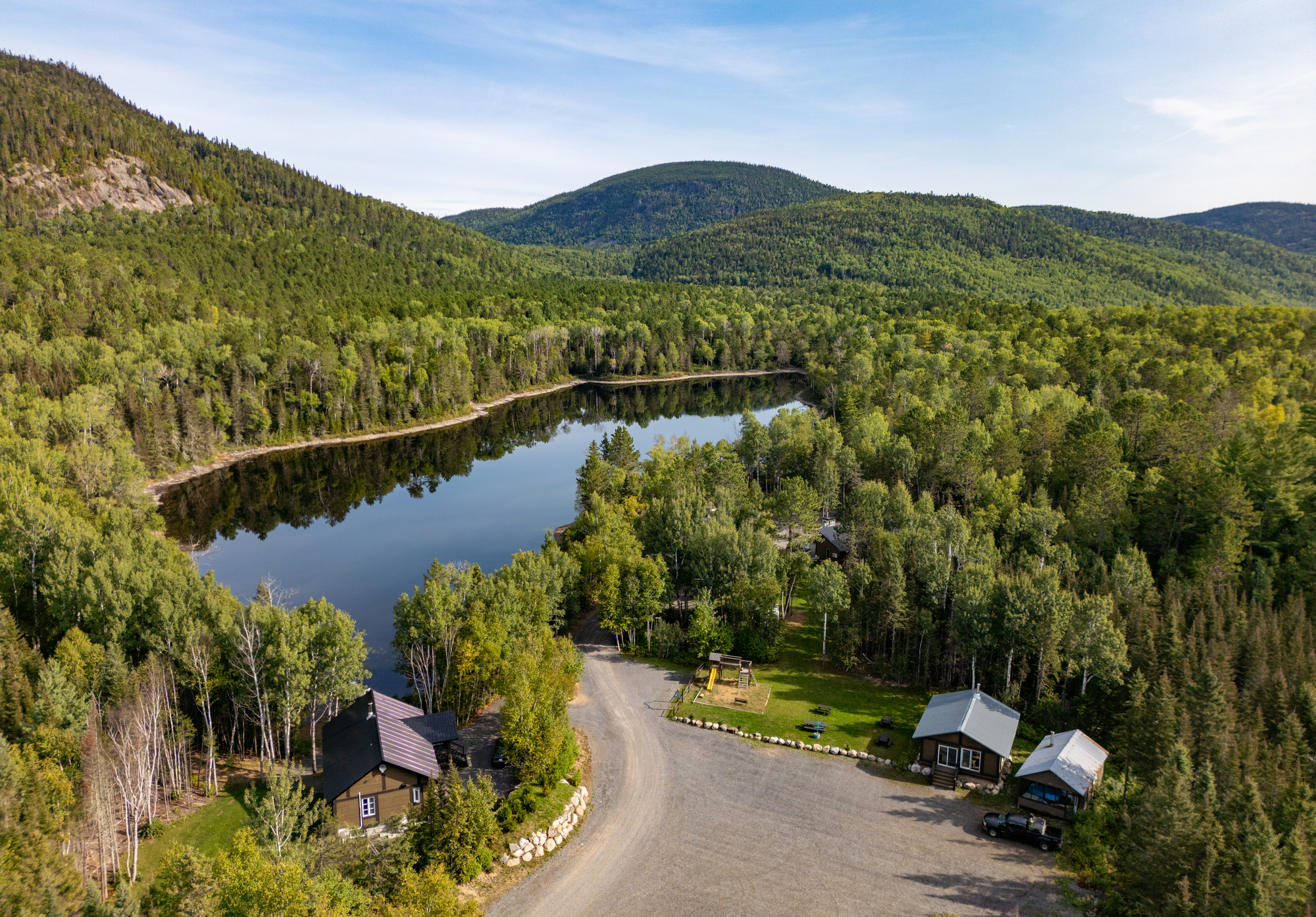 Vue aérienne du Domaine Le Pic-Bois avec chalets et lac entouré de forêts verdoyantes dans la région de Charlevoix