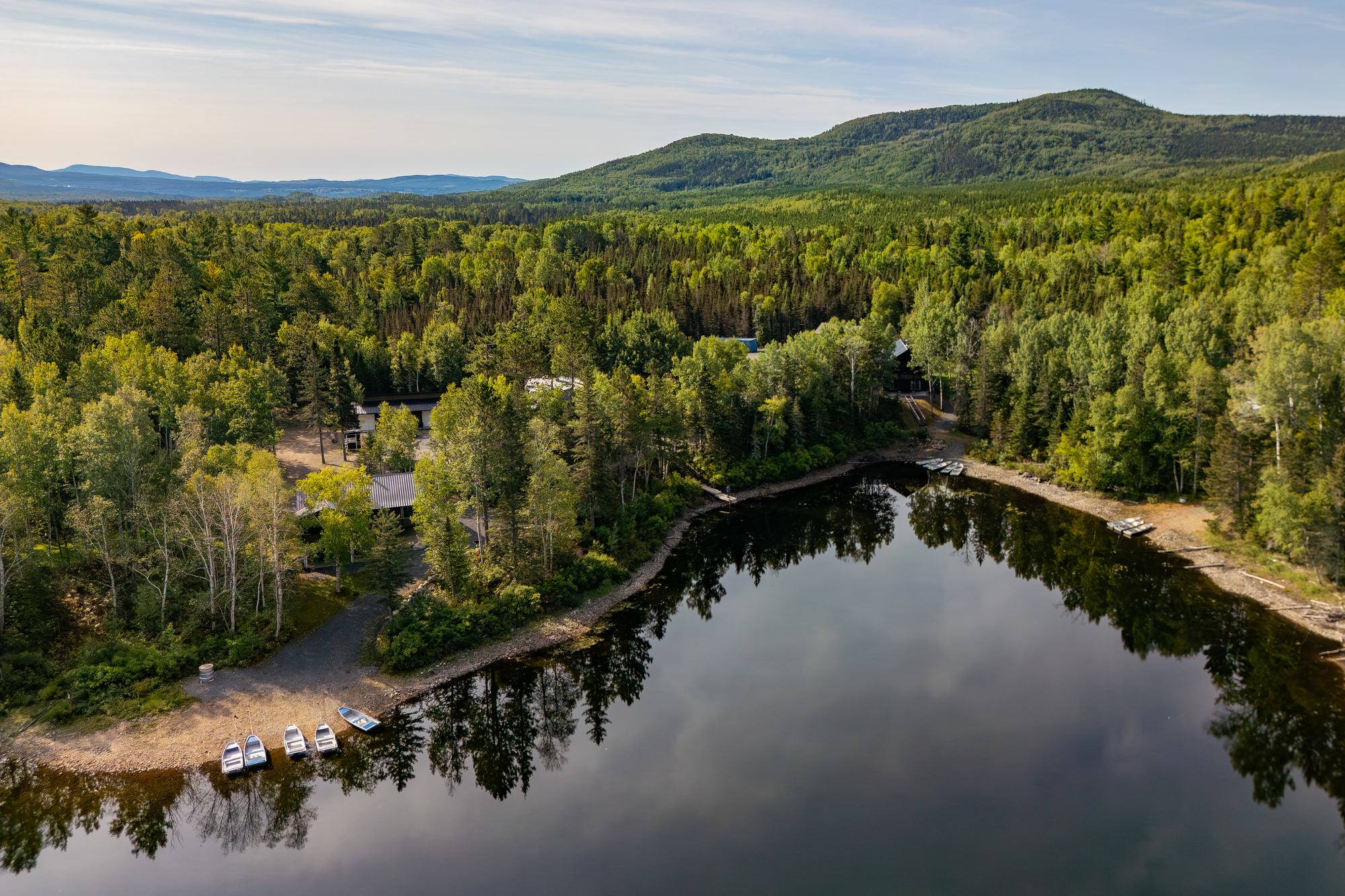 Vue aérienne d'un plan d'eau bordé d'arbres, avec des chalets et des bateaux au Domaine Le Pic-Bois à Charlevoix