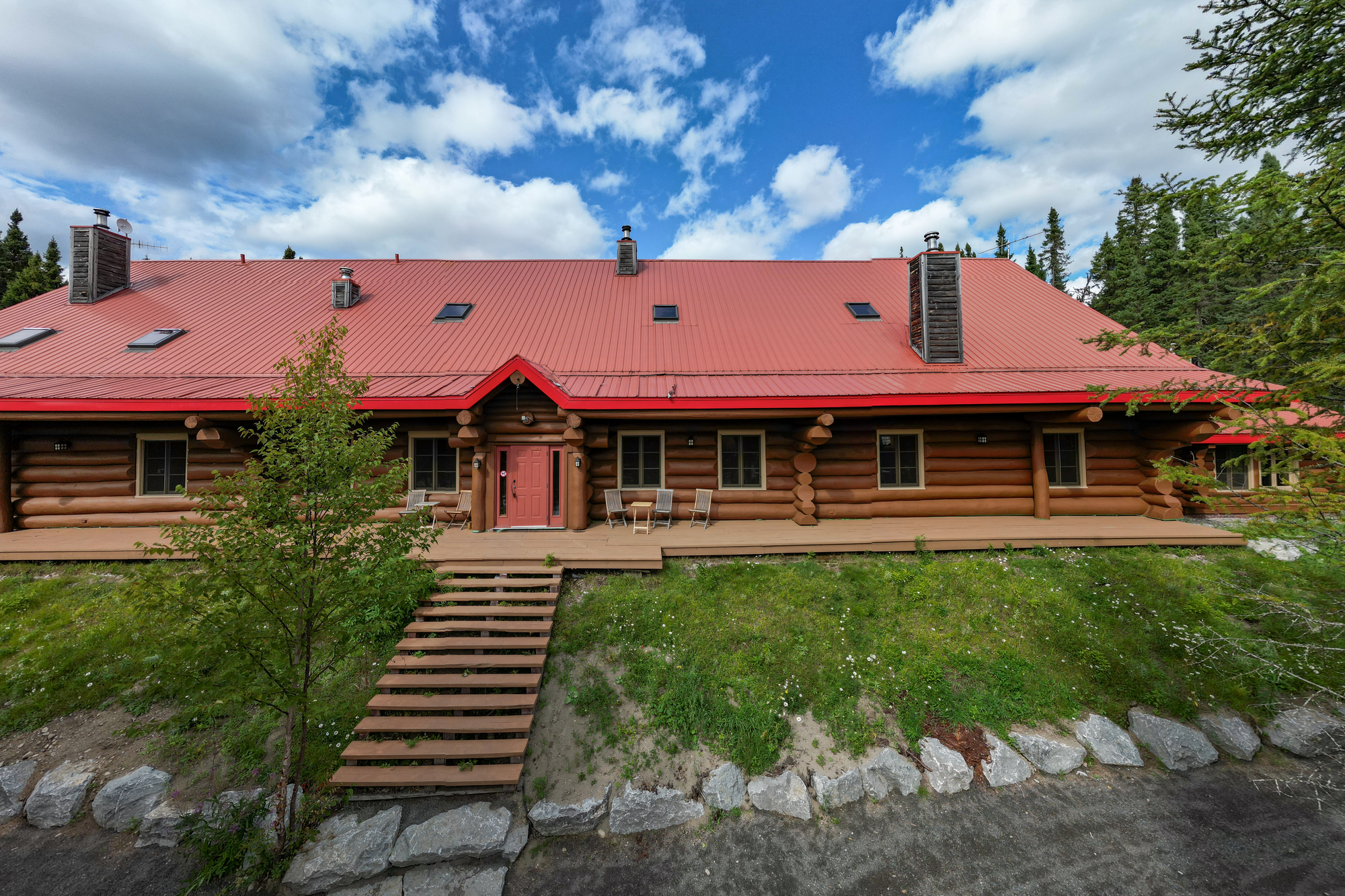 Auberge en rondins avec toit rouge entourée d'arbres dans un environnement naturel à la pourvoirie du Lac Moreau