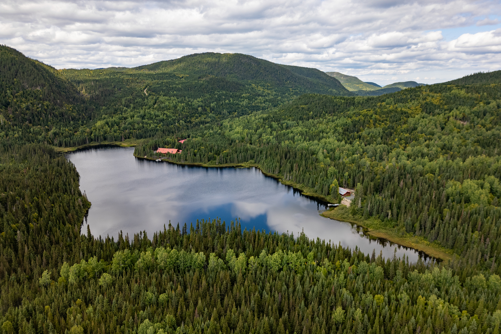 Lac entouré de forêts verdoyantes et de collines, avec des chalets visibles près de l'eau à la pourvoirie du Lac Moreau