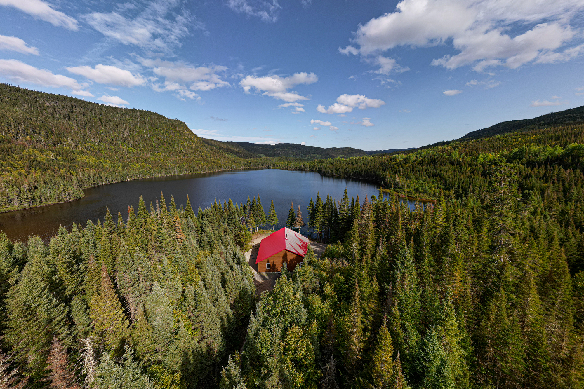 Vue aérienne d'un chalet rouge entouré de forêts et d'un lac, typique de la pourvoirie du Lac Moreau en Charlevoix