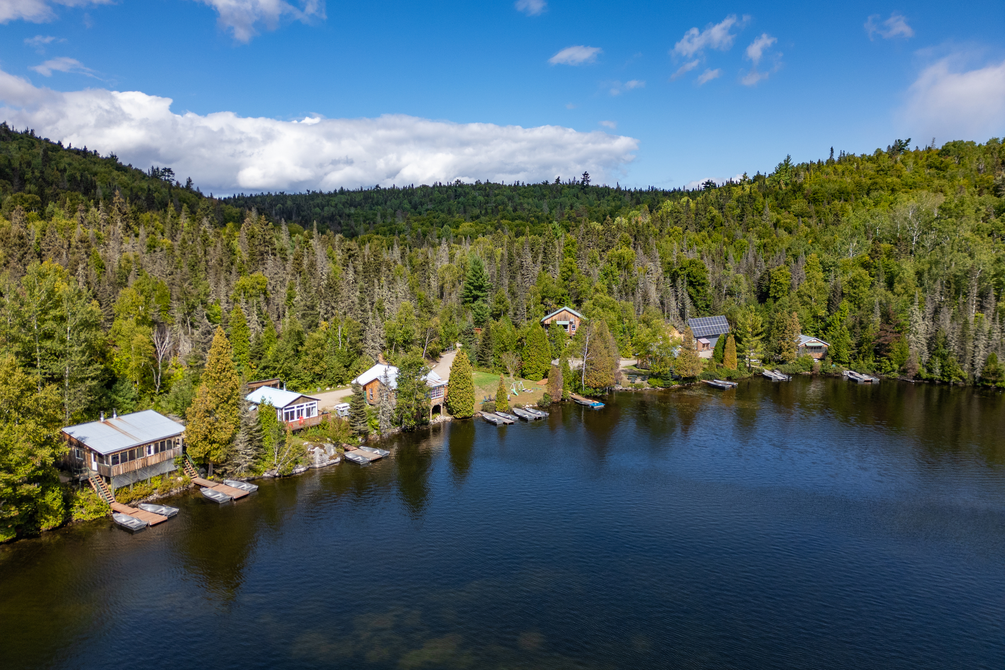 Chalets en bordure d'un lac entourés de forêts verdoyantes sous un ciel bleu, près de la Pourvoirie Baie-Sainte-Catherine