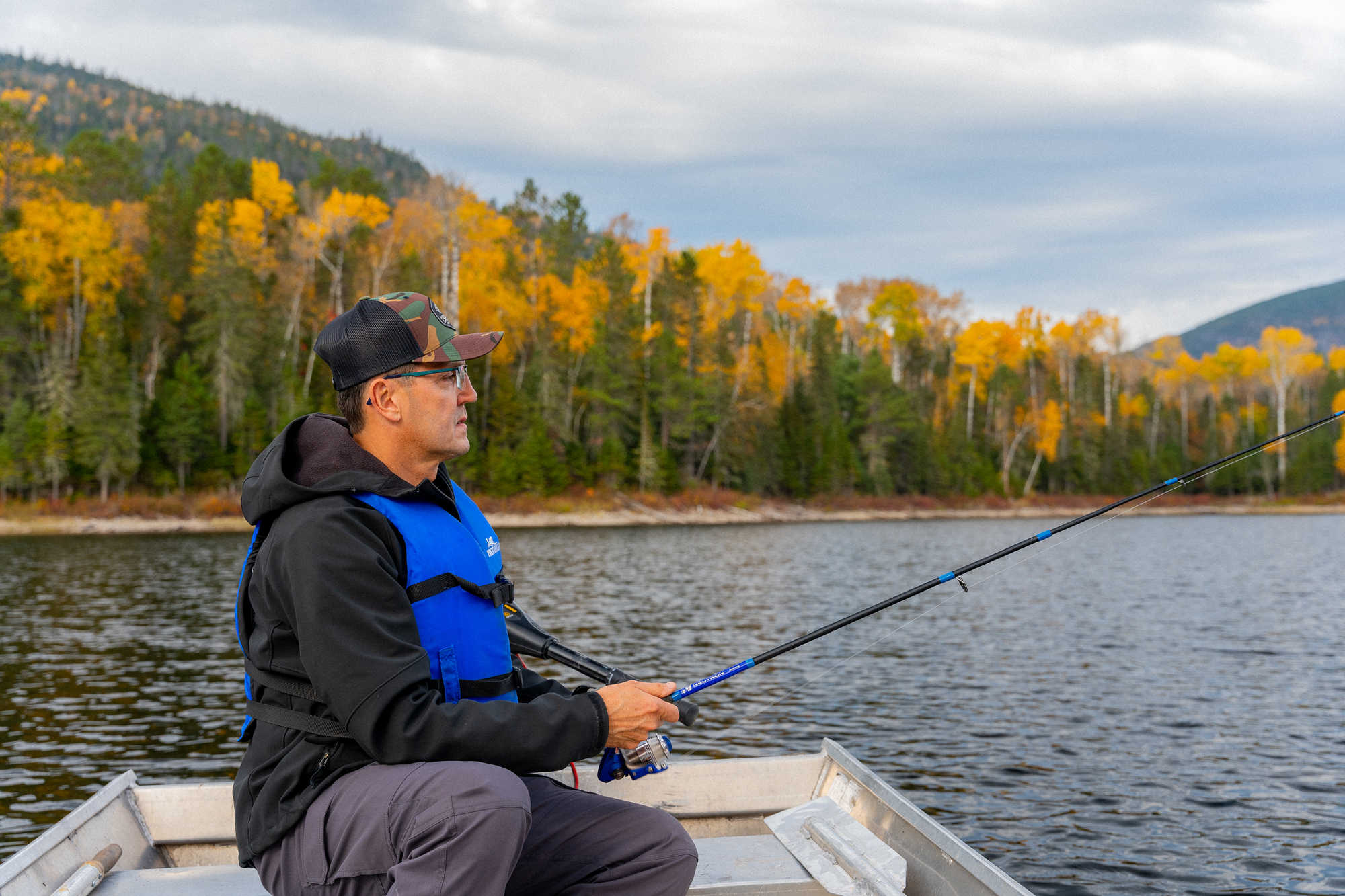 Person fishing from a small boat on a lake surrounded by autumn trees in Charlevoix