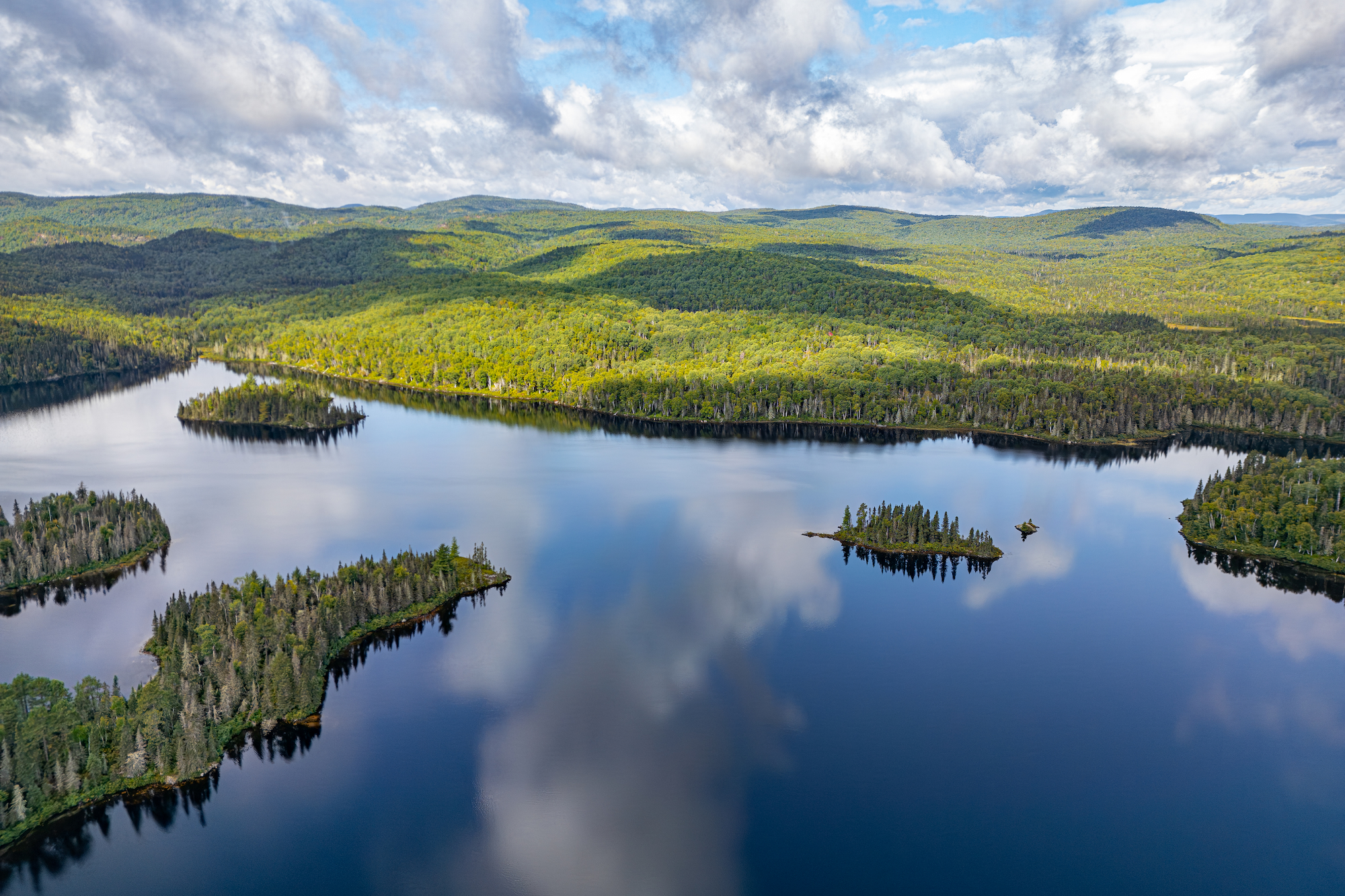 Lush green forested islands surrounded by calm blue waters under a partly cloudy sky in Charlevoix region