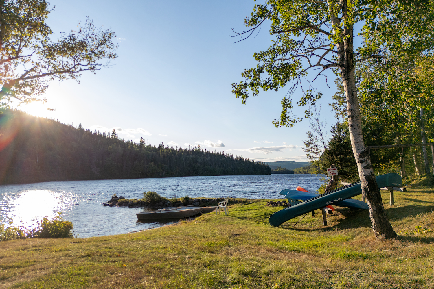 Riverbank scene at Domaine Chasse et Pêche Gaudias Foster with canoes, grass, and mountains in the background under sunny sky