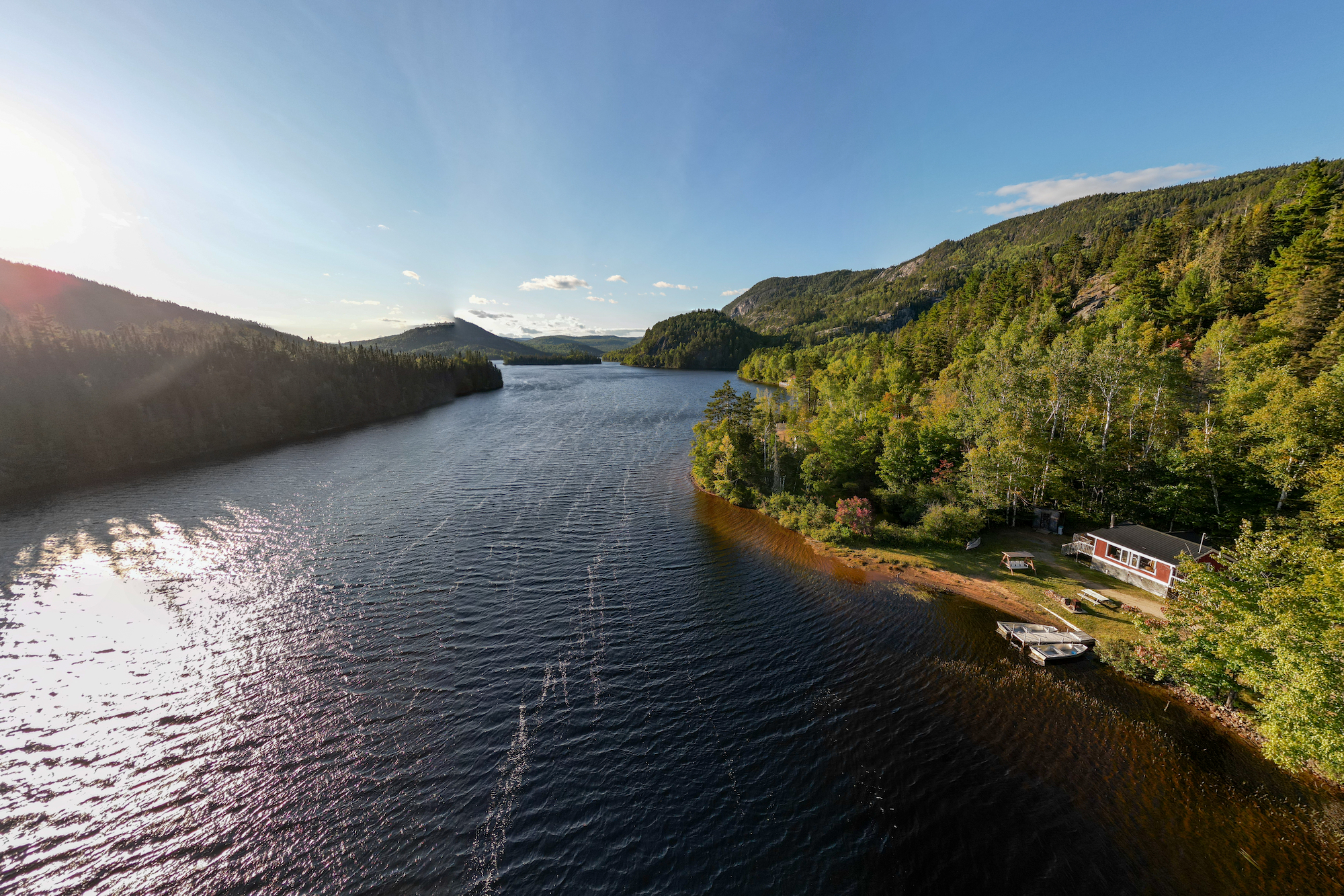 Lac bordé de forêts, avec un chalet et une barque sur la rive, montagnes en arrière-plan dans la région de Charlevoix