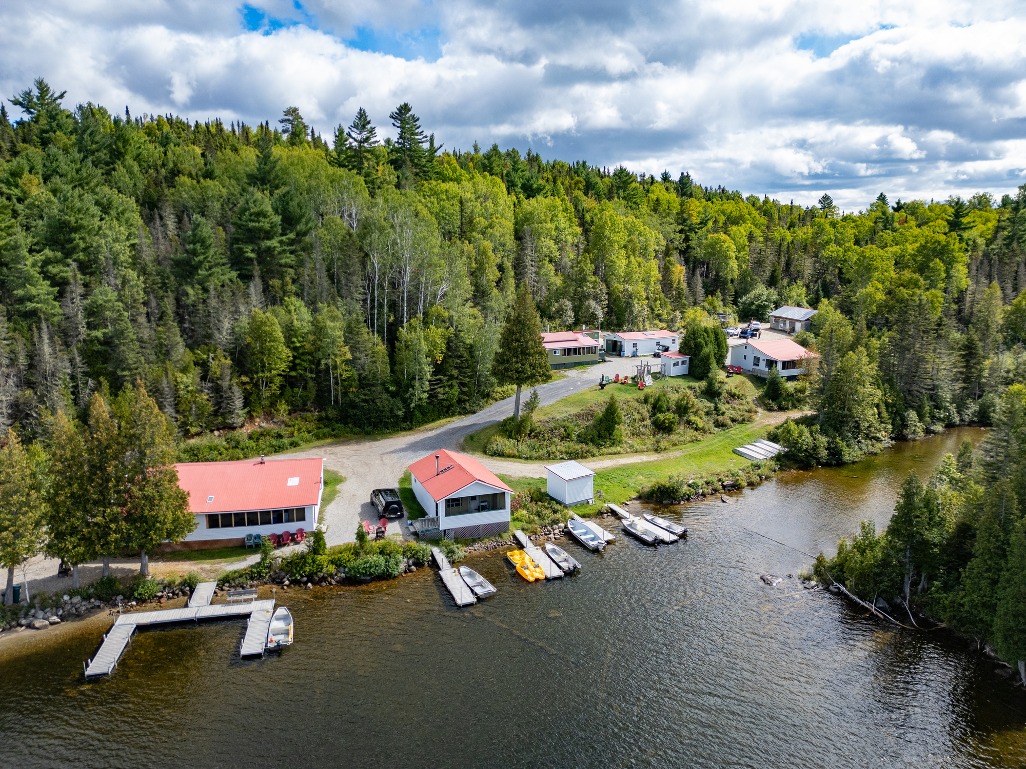Aerial view of Humanity Lodge with cabins, a dock, and kayaks along a serene river surrounded by lush trees