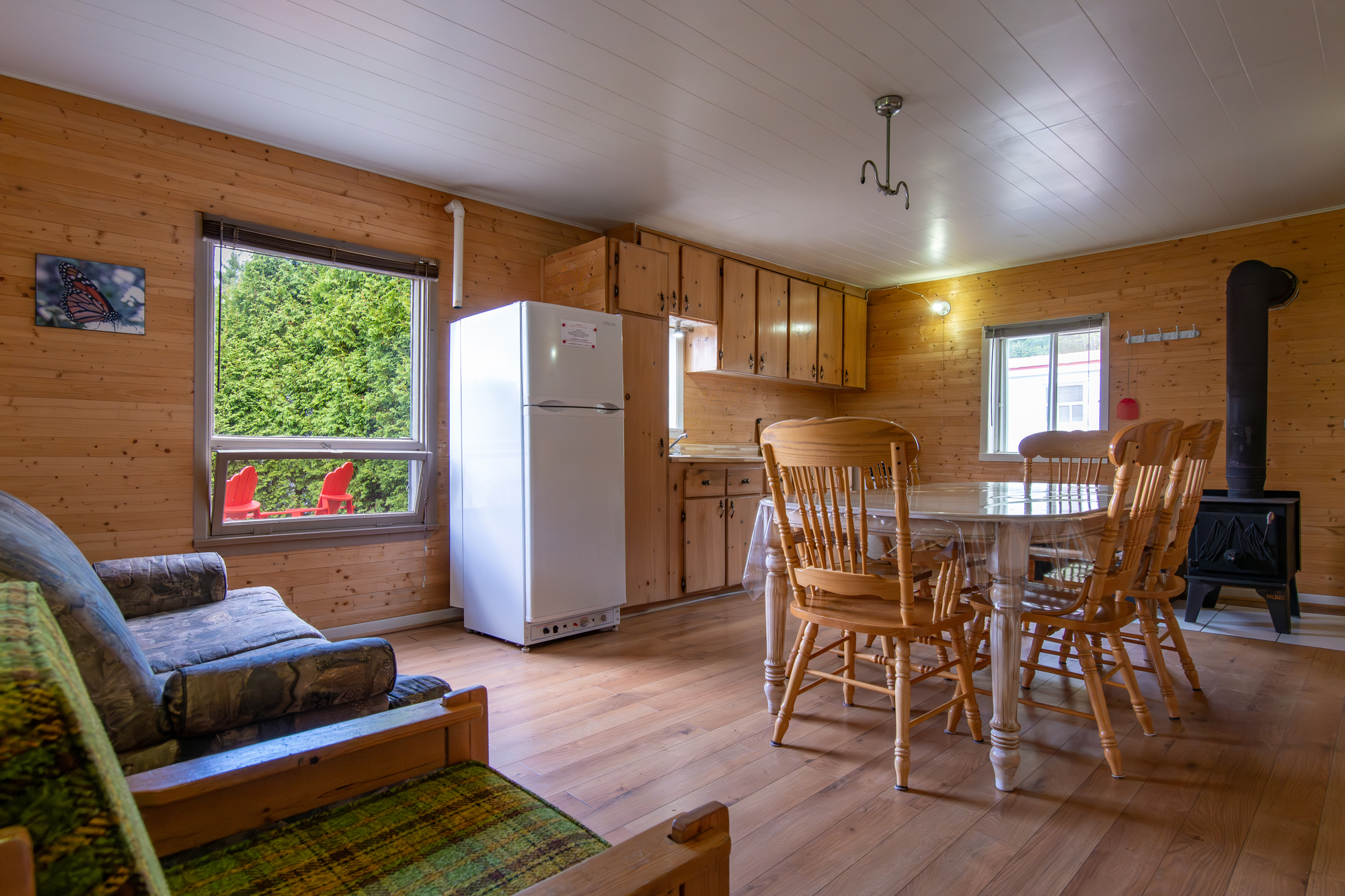 cozy cabin interior featuring wooden walls, a dining table, chairs, a sofa, and a refrigerator, ideal for tranquil getaways