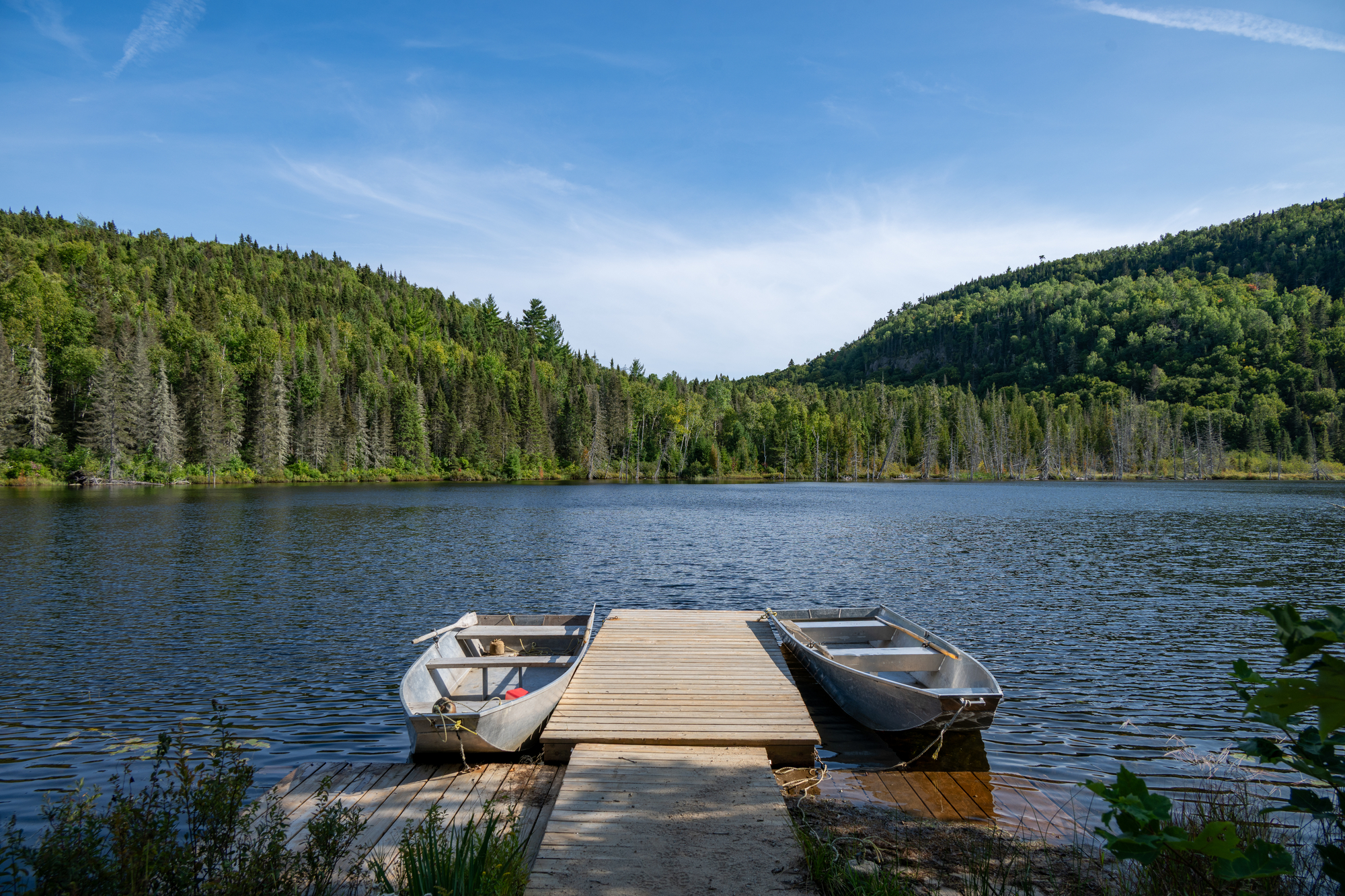Quai en bois au bord d'un lac entouré de forêts verdoyantes et de collines dans la région de Charlevoix