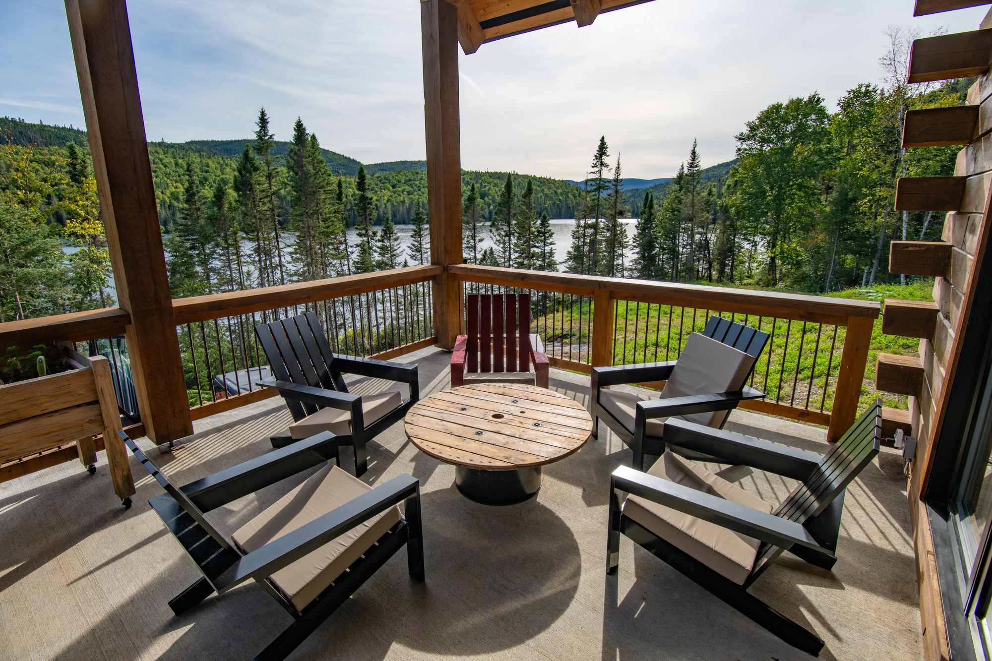 Outdoor seating area with black chairs and a round wooden table overlooking a serene lake and forest in Charlevoix