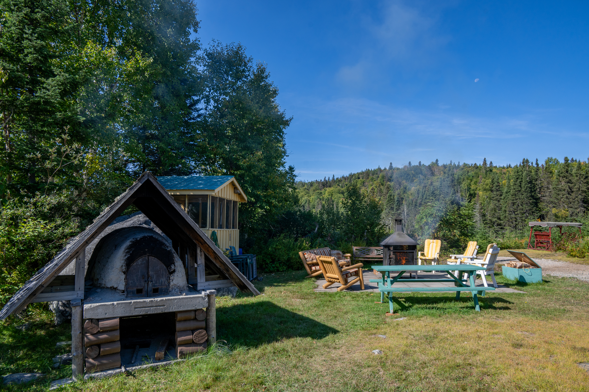 Cabin with outdoor seating and wood-fired oven in a serene wilderness setting at Pourvoirie du Lac Croche in Charlevoix