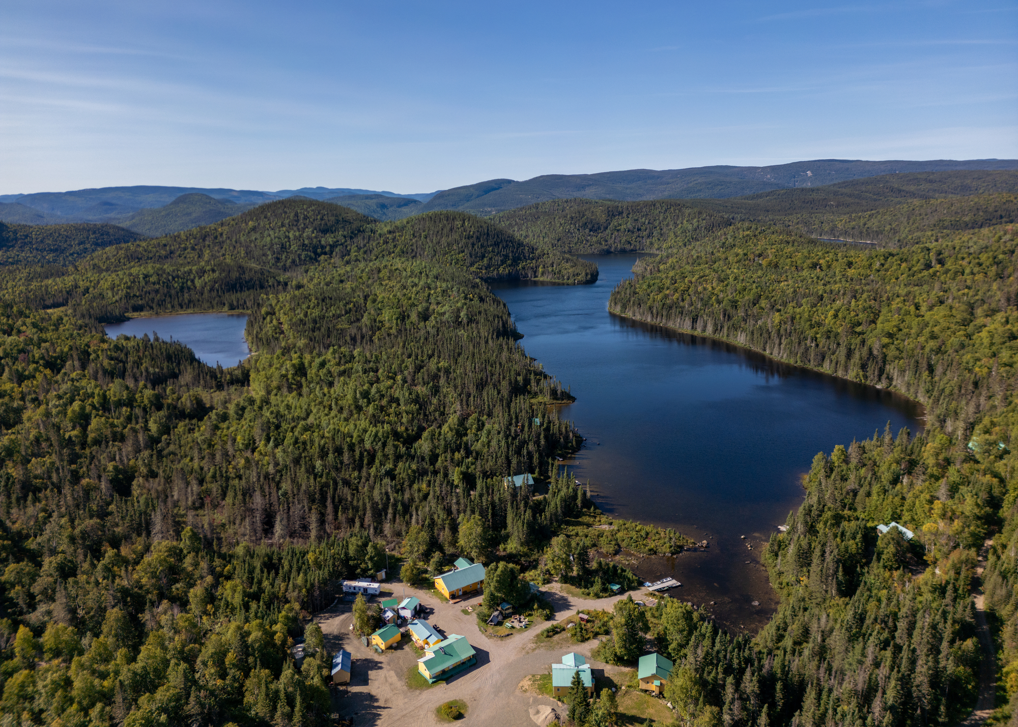Vue aérienne de la pourvoirie du Lac Croche entourée de montagnes et de forêts, avec des lacs et installations en bas
