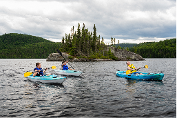 Trois personnes en kayak sur un lac entouré de forêts, avec une petite île en arrière-plan dans la région de Charlevoix