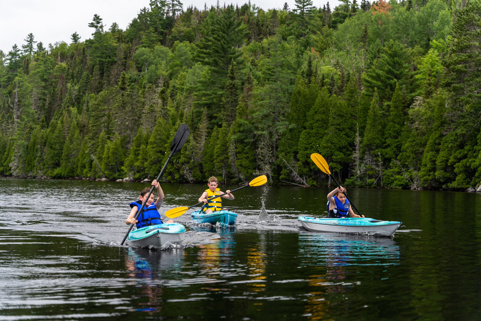Trois enfants en kayak sur un lac entouré de forêts verdoyantes, profitant d'une activité de plein air en famille