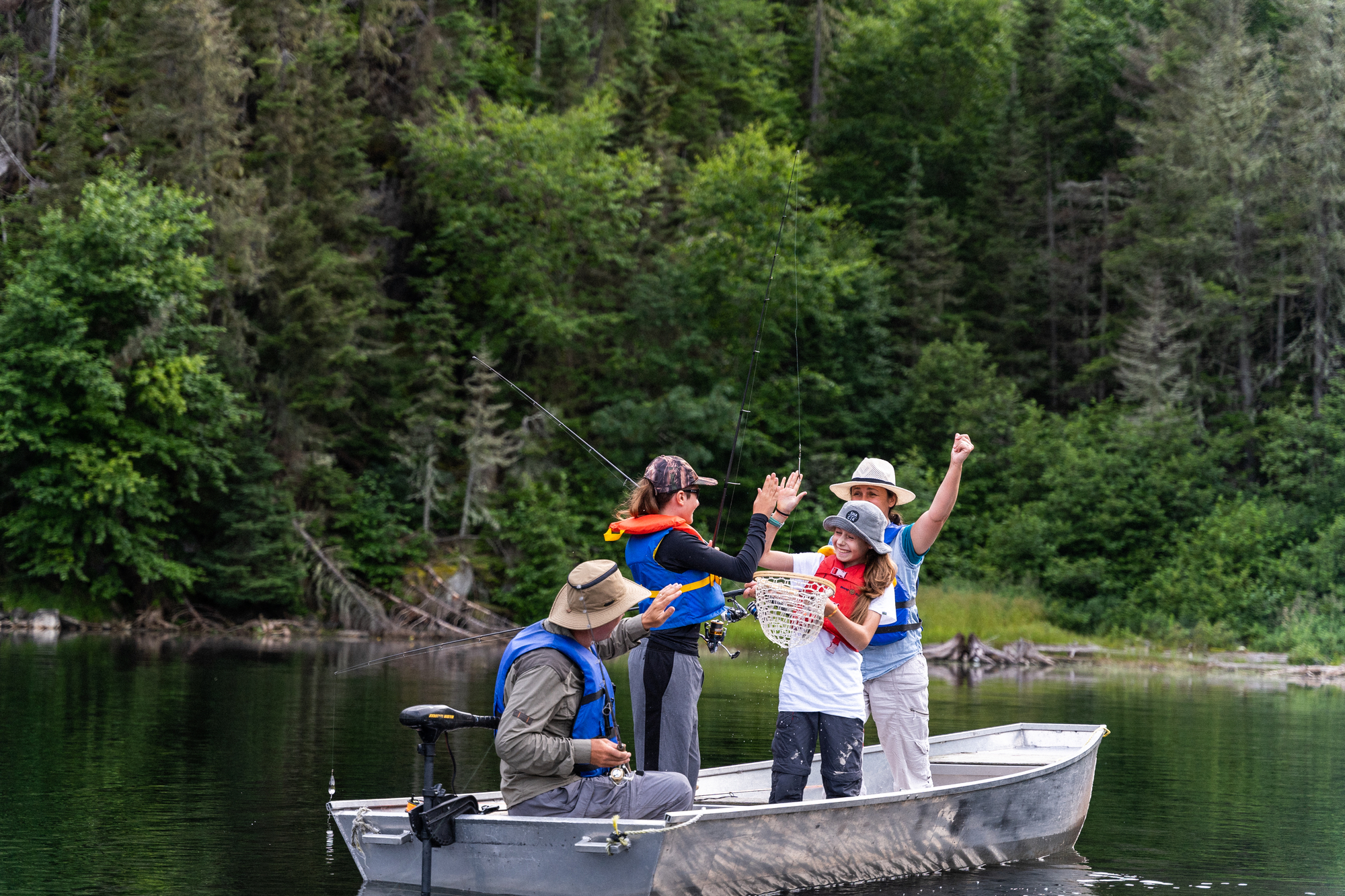 Group of four people fishing from a small boat in a serene lake surrounded by lush greenery in Charlevoix