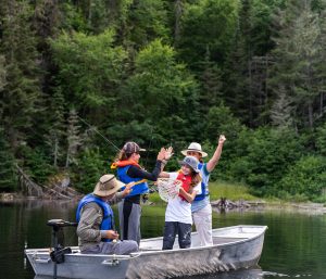 Groupe familial en canot, souriant et célébrant une prise de pêche dans un cadre naturel verdoyant