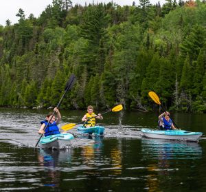 Trois personnes en kayak sur un lac entouré de forêt verdoyante, profitant d'une activité en plein air au cœur de Charlevoix