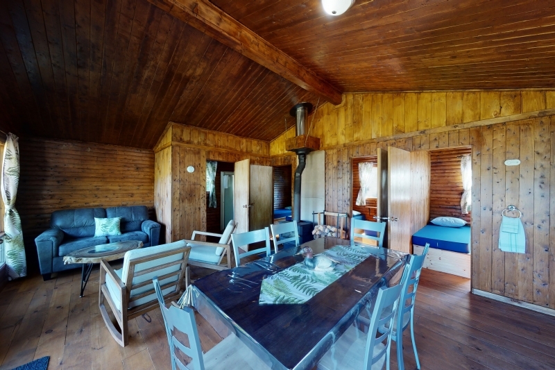 cozy wooden cabin interior with dining area, seating, and two closed bedrooms at Domaine Comporté near La Malbaie
