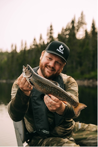 Homme souriant en bateau tenant une truite dans un environnement forestier de Charlevoix