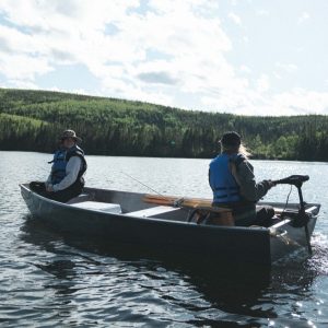Deux personnes dans une barque sur un lac, portant des gilets de sauvetage, entourées de forêts verdoyantes