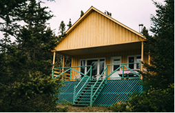 Cabane en bois au bord des arbres, avec une terrasse en bois vert, typique des pourvoiries de Charlevoix