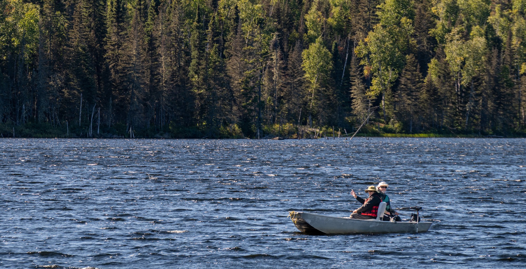 Deux personnes pêchent en bateau sur un lac entouré de forêts verdoyantes dans la région de Charlevoix