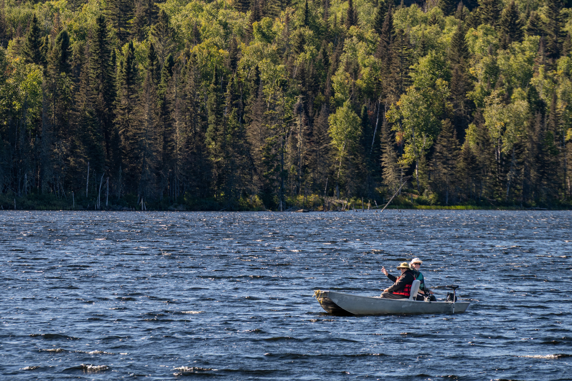 Deux personnes pêchent en bateau sur un lac entouré de forêts dans la région de Charlevoix