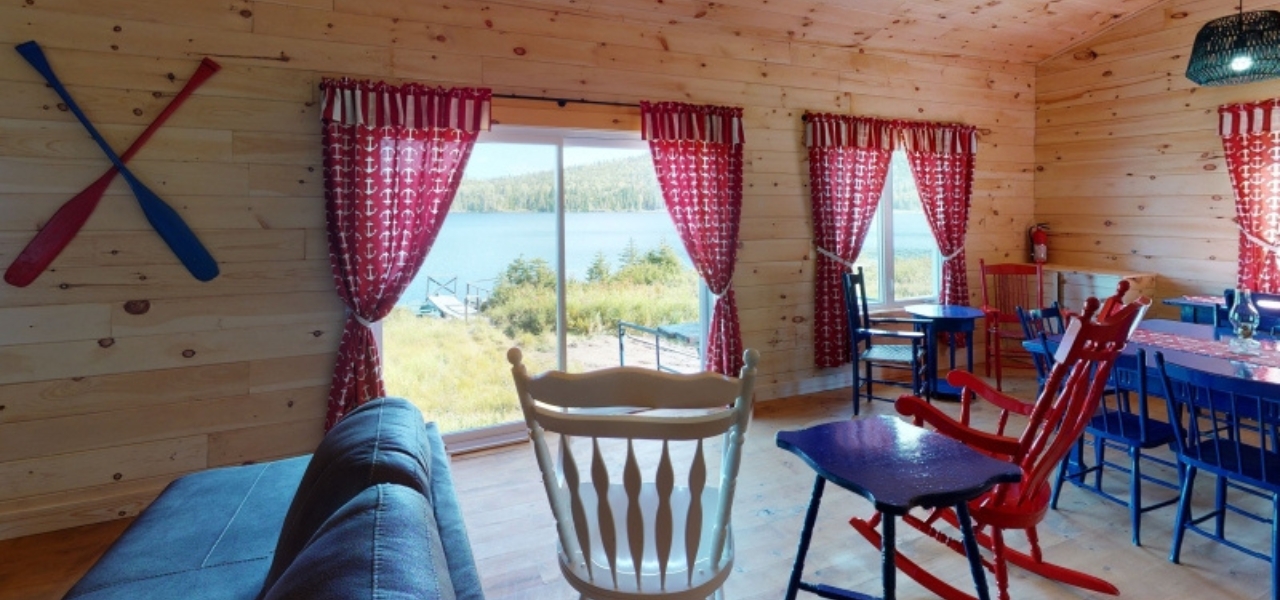 Chalet en bois avec vue sur le lac, fenêtres avec rideaux rouges à motifs, fauteuils colorés et coin repas lumineux
