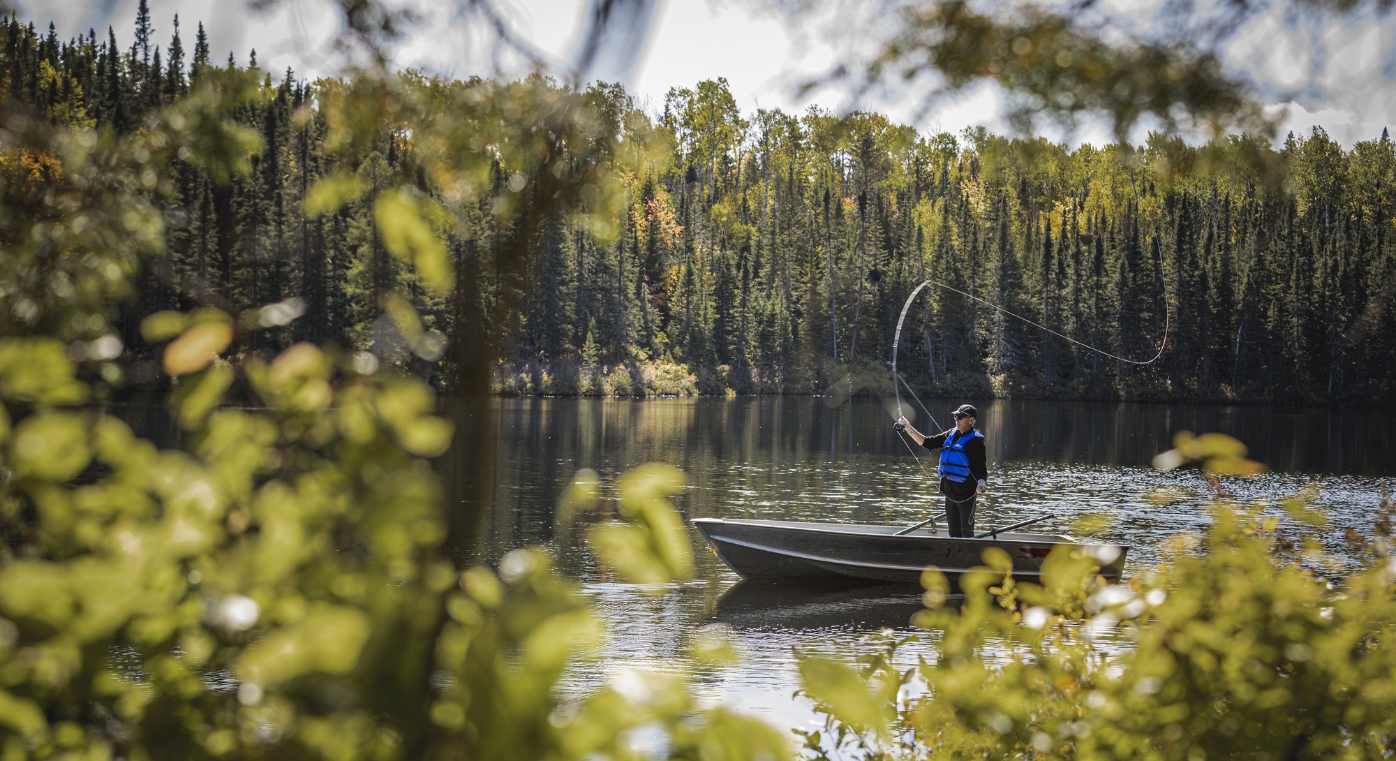 Homme en train de pêcher depuis un bateau sur un lac entouré de forêts en automne dans la région de Charlevoix