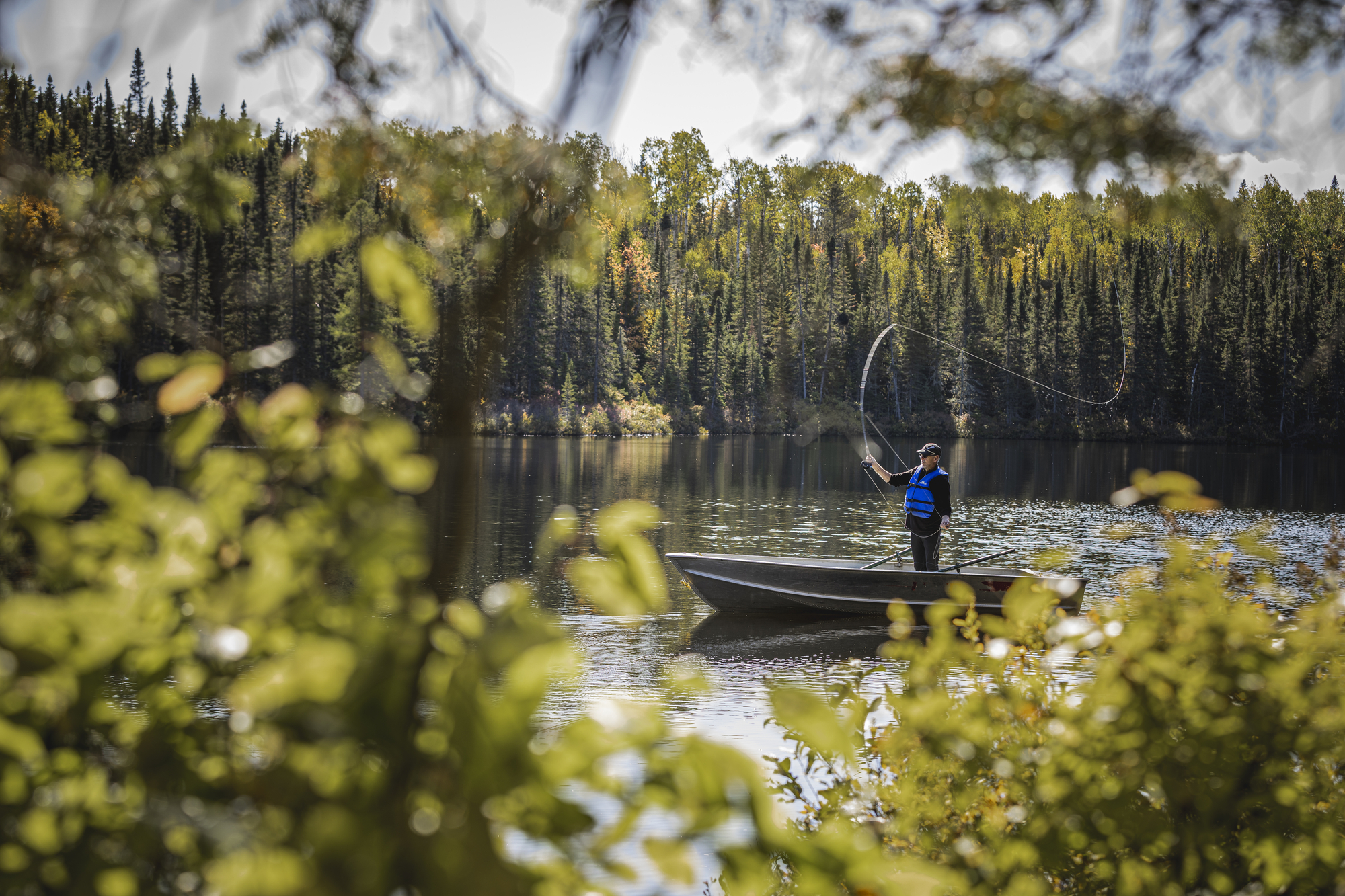 Pêcheur sur un bateau au milieu d'un lac entouré d'arbres en automne avec une canne à pêche en main