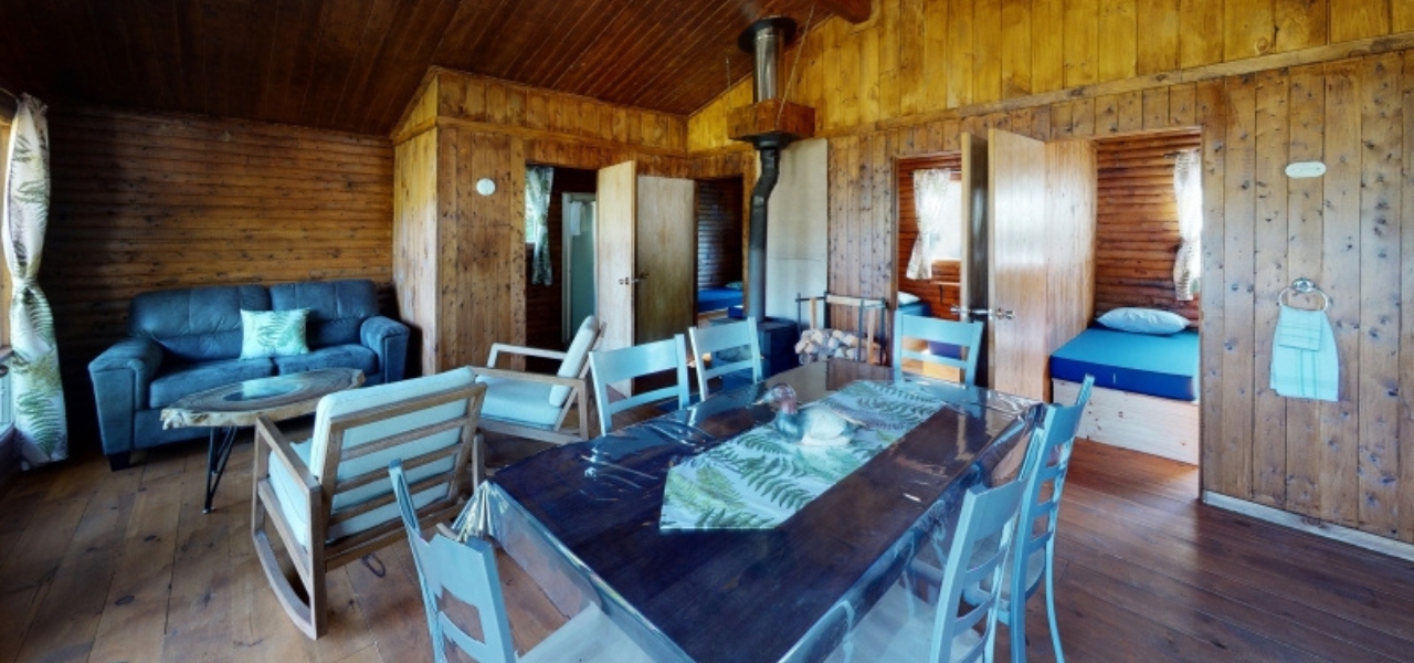 Chalet en bois avec salon, table à manger et chambres, idéal pour un séjour de pêche à la truite mouchetée