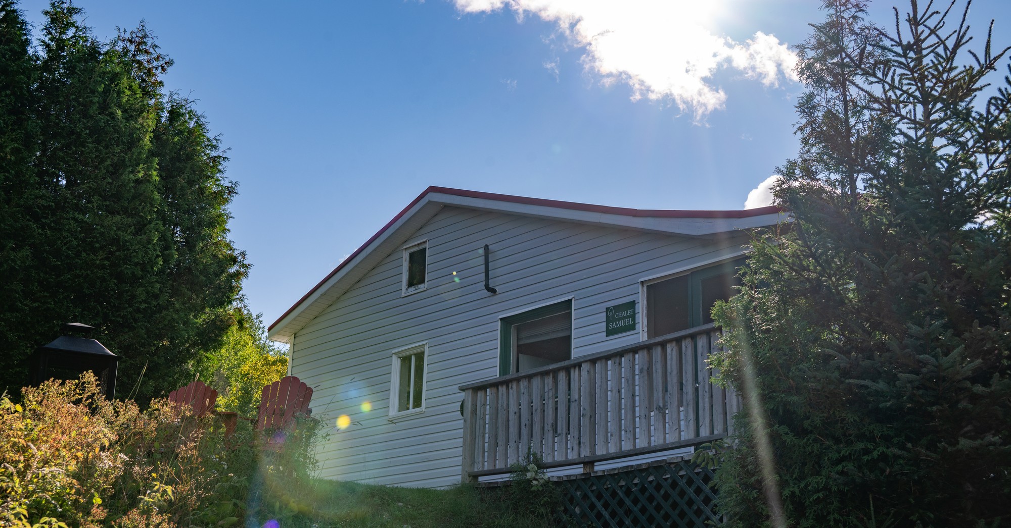 Chalet en bois avec balcon entouré de verdure sous un ciel ensoleillé à la Pourvoirie Humanité pour la pêche d'automne