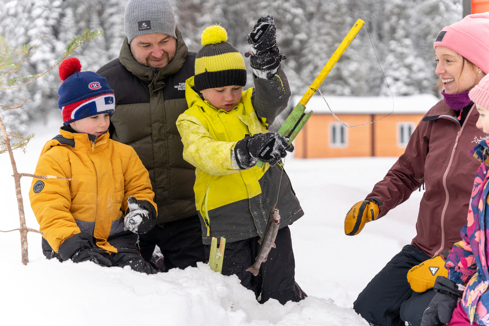 Enfants et adultes s'amusent dans la neige, préparant du matériel pour la pêche blanche en famille au Domaine Le Pic-Bois
