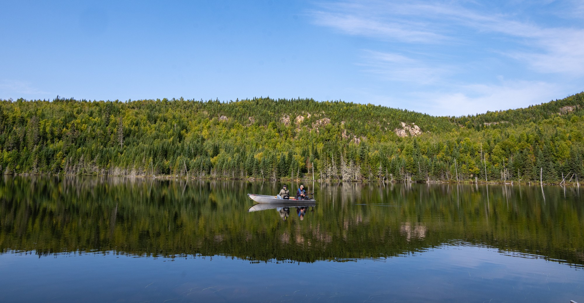 bateau sur un lac calme entouré de forêts verdoyantes, idéal pour la pêche aux grosses truites à Charlevoix