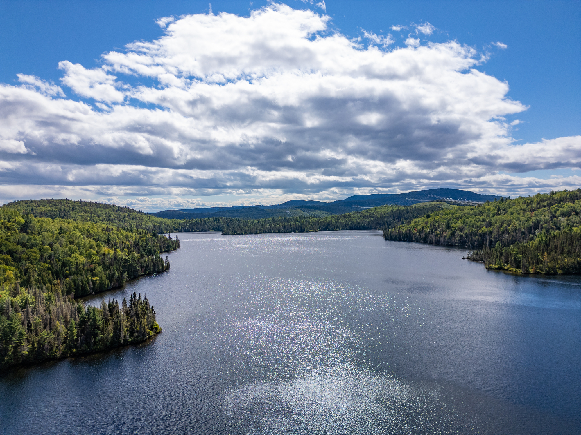 Lac serein entouré de forêts verdoyantes sous un ciel nuageux, idéal pour la pêche à Baie-Sainte-Catherine
