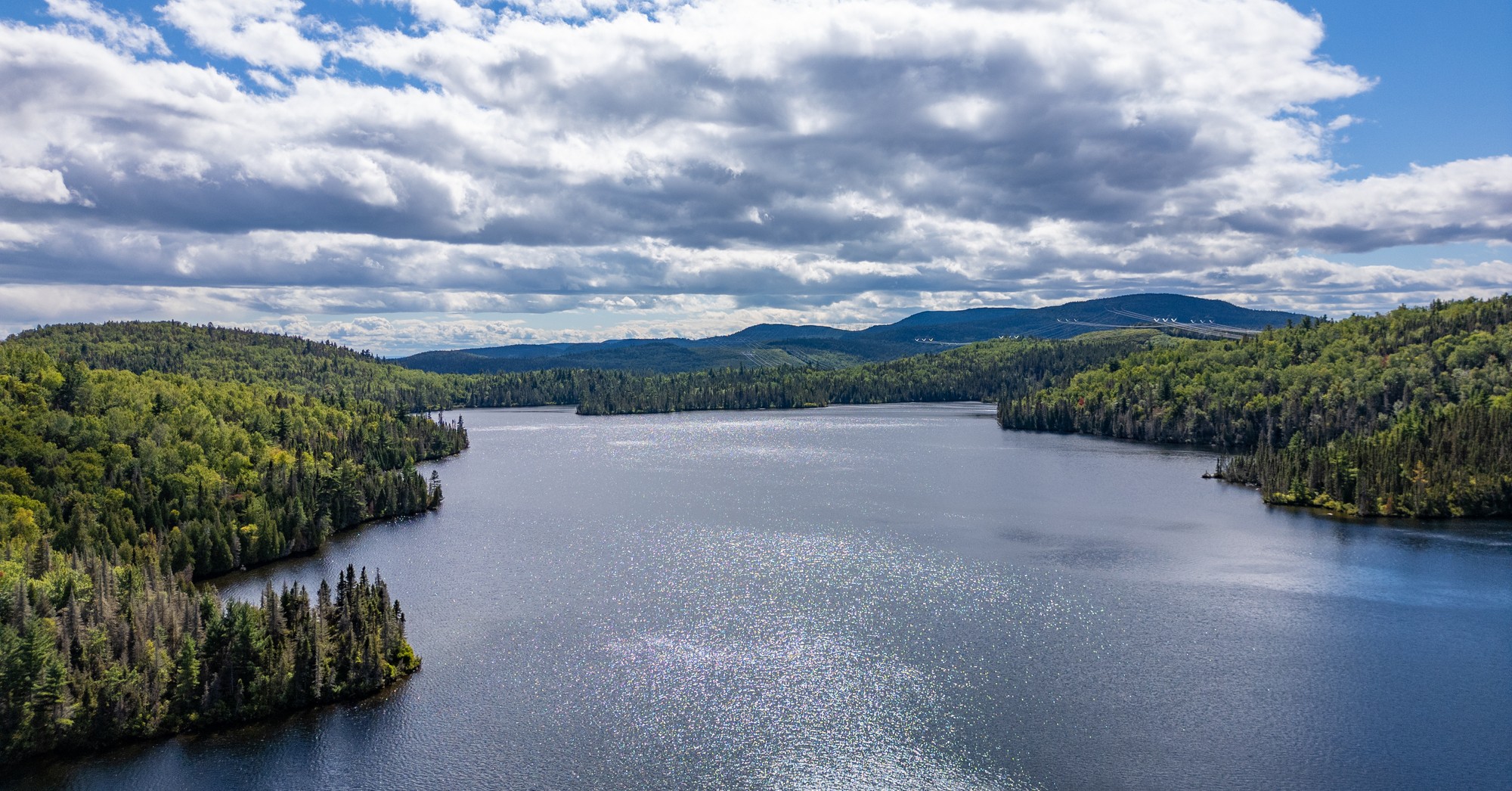 Lac entouré de forêts verdoyantes sous un ciel nuageux, parfait pour la pêche à Baie-Sainte-Catherine