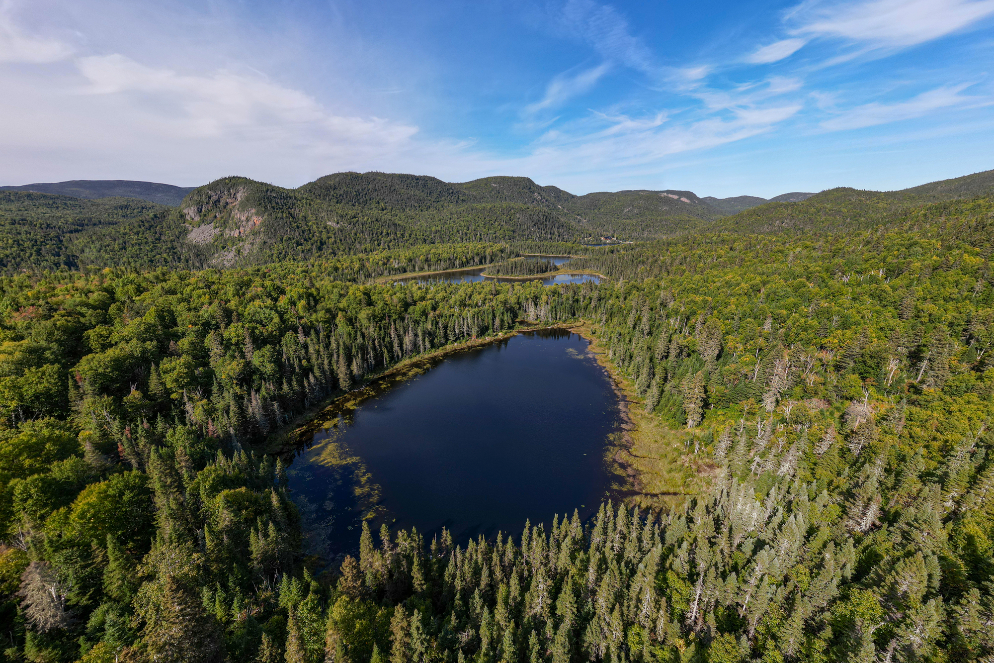 Lac entouré de forêts luxuriantes dans un paysage sauvage de Charlevoix, idéal pour la petite chasse au Domaine du Lac Brouillard