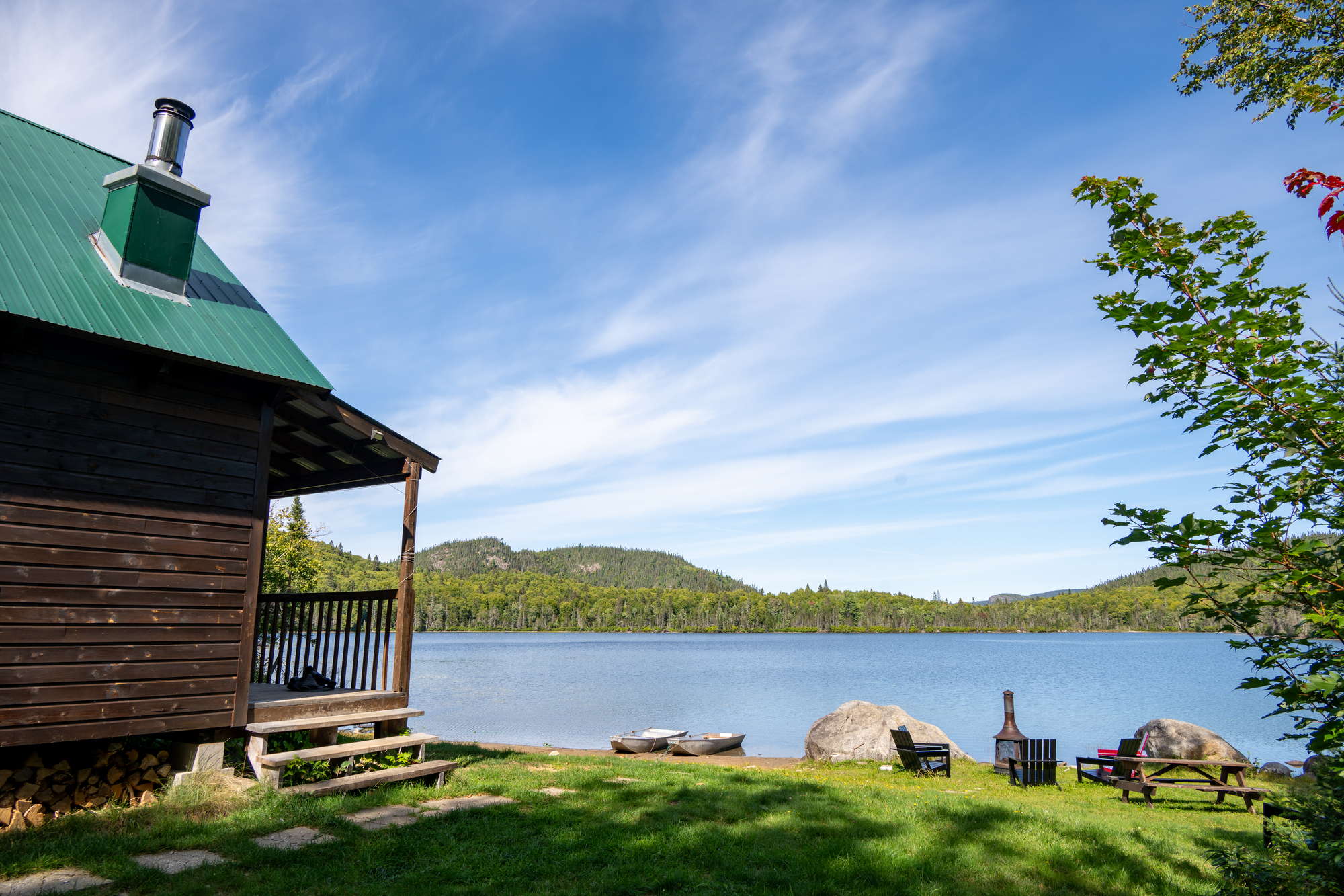 Cabane en bois surplombant un lac entouré de forêts, ciel bleu parsemé de nuages, cadre paisible pour la chasse