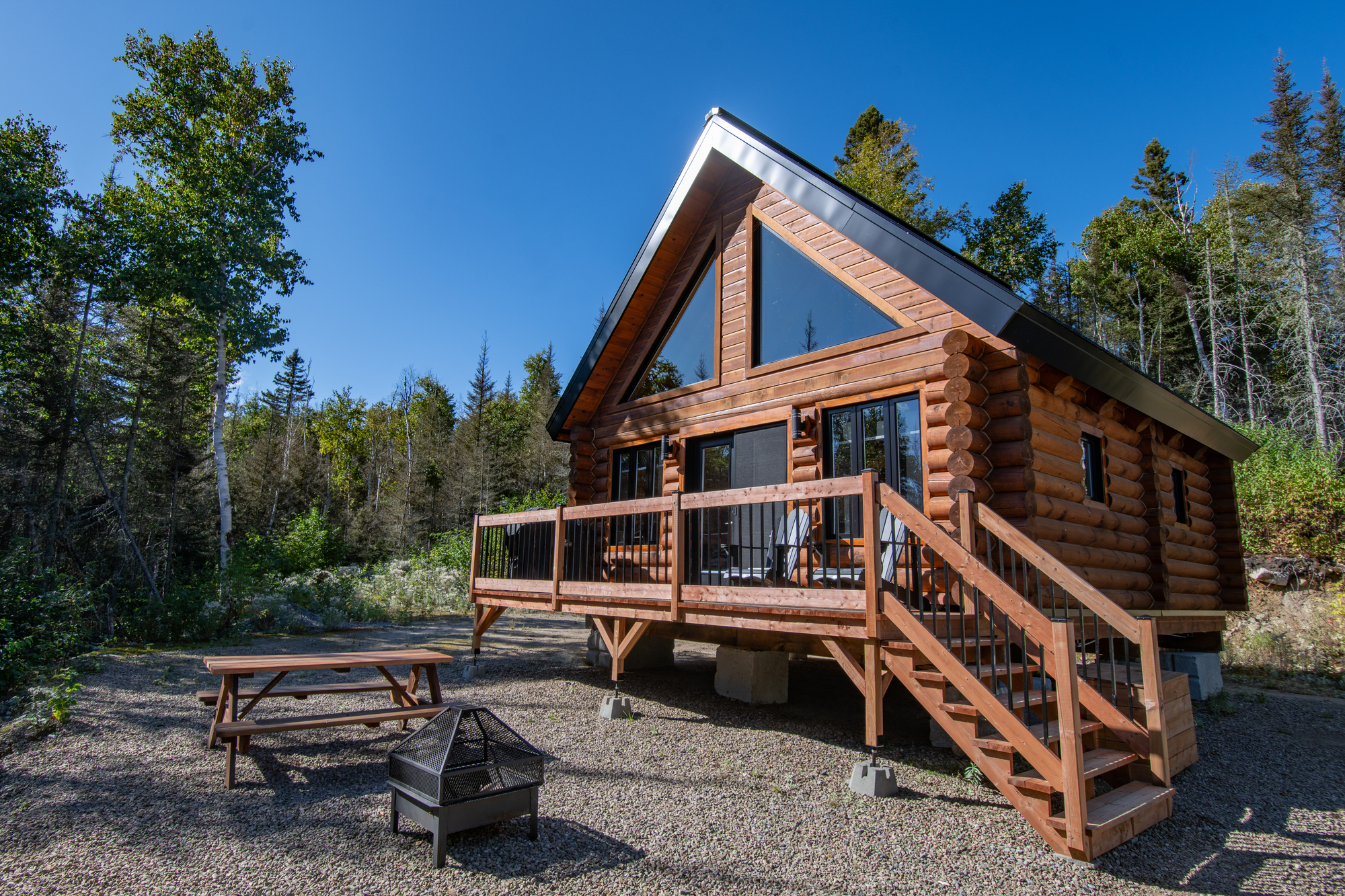 Chalet en bois rond avec grande terrasse, entouré de végétation, idéal pour un séjour de pêche dans Charlevoix