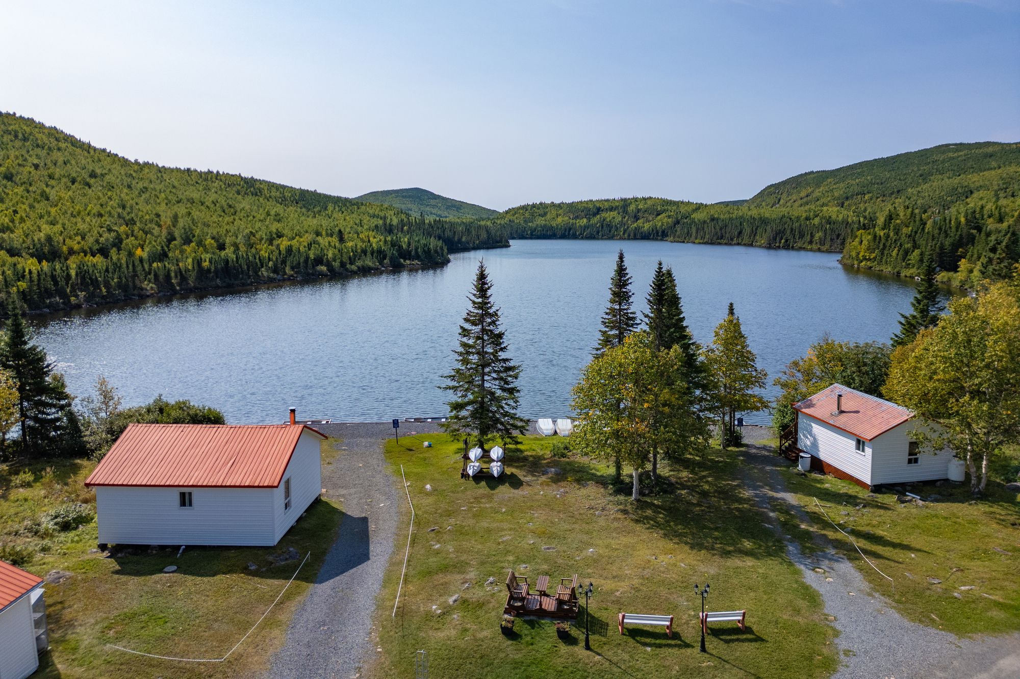 Vue aérienne de chalets au bord d'un lac entouré de forêts, lieu idéal pour des vacances en famille à Charlevoix