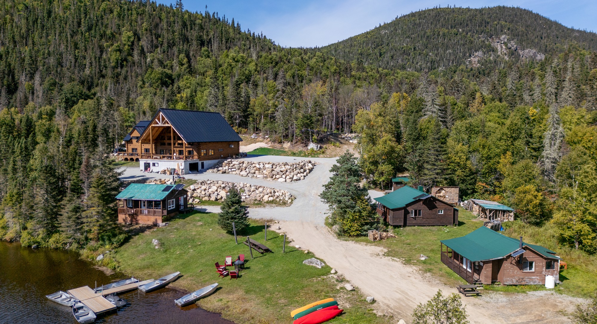 Vue aérienne du Domaine du Lac Brouillard avec hébergement et embarcations au bord d'un lac entouré de forêt verte