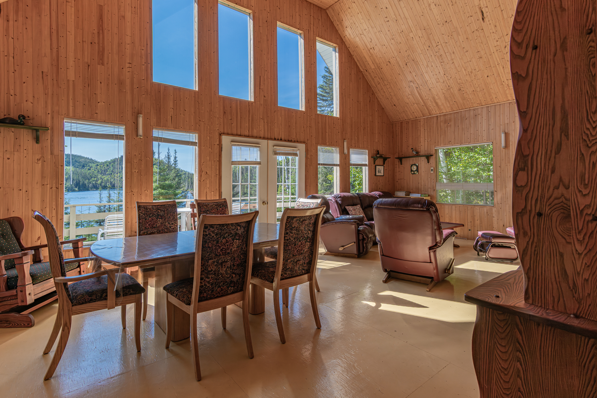 Intérieur en bois d'un chalet lumineux avec fenêtres panoramiques sur le paysage, table à manger et chaises confortables