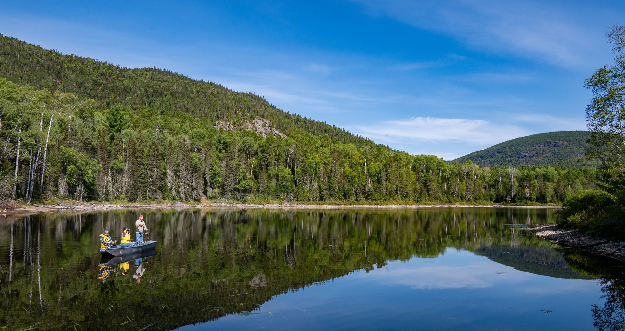 bateau sur un lac tranquille entouré de montagnes verdoyantes, ciel bleu et reflet des arbres dans l'eau