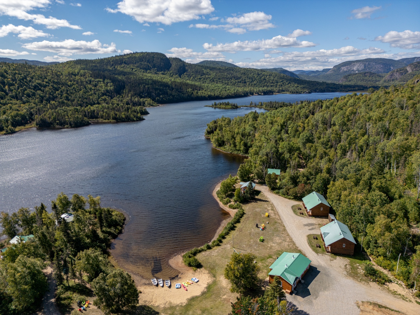 Aerial view of a serene lake surrounded by lush forests and outfitter cabins, ideal for a nature getaway in Charlevoix